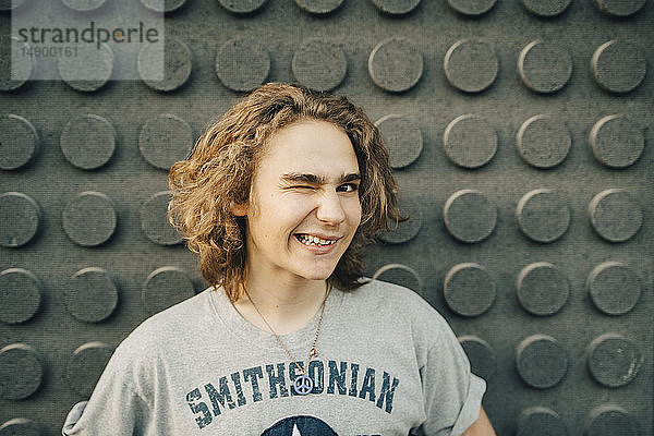 Porträt eines lächelnden jungen Mannes  der mit einem Augenzwinkern an die Wand winkt