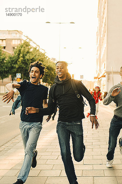 Glückliche spielerische Freunde laufen auf der Straße in der Stadt