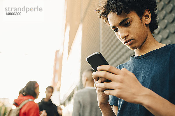 Teenager  der ein Mobiltelefon benutzt  während Freunde auf der Straße im Hintergrund stehen