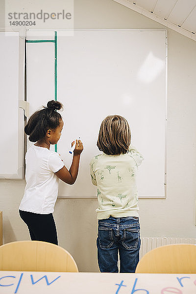 Rückansicht eines Jungen und eines Mädchens  die in der Grundschule auf einer Tafel schreiben