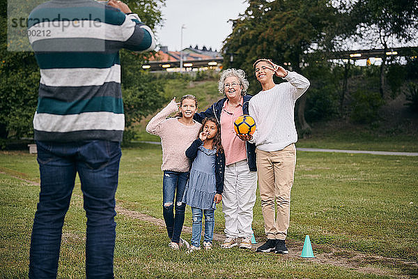 Ein Mann fotografiert glückliche Großmutter und Enkelkinder  die während des Picknicks im Park ein Friedenszeichen gestikulieren