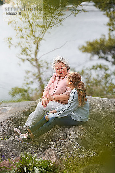 Großmutter und Enkelin unterhalten sich  während sie auf einem Felsen im Park sitzen