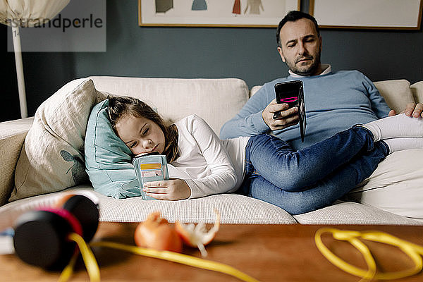 Vater und Tochter benutzen Mobiltelefone auf der Couch im Wohnzimmer