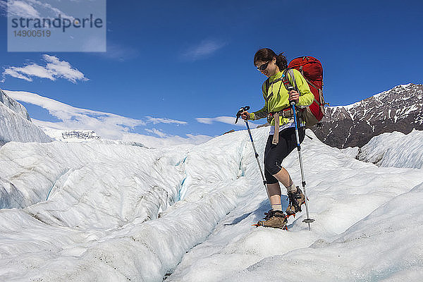 Frau  die im Sommer mit dem Rucksack über den Root-Gletscher mit Steigeisen zum Donoho Peak wandert  Wrangell Mountains  Wrangell-St. Elias National Park  Süd-Zentral-Alaska; Kennicott  Alaska  Vereinigte Staaten von Amerika