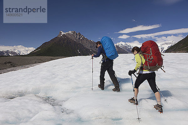 Mann und Frau wandern im Sommer mit Steigeisen über den Root-Gletscher in Richtung Donoho Peak  Wrangell Mountains  Wrangell-St. Elias National Park  Süd-Zentral-Alaska; Kennicott  Alaska  Vereinigte Staaten von Amerika