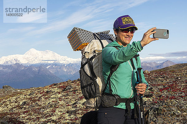 Frau macht ein Selfie während einer Rucksacktour mit Denali im Hintergrund  entlang des Kesugi Ridge Trail  Denali State Park an einem sonnigen Herbsttag  Southcentral Alaska  USA