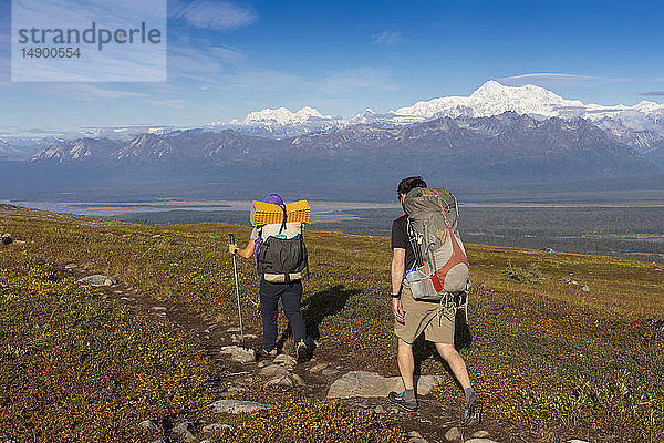 Frau und Mann wandern mit dem Rucksack auf der Tundra in Richtung Denali und Alaska Range  entlang des Kesugi Ridge Trail  Denali State Park  an einem sonnigen Herbsttag  Süd-Zentral-Alaska; Alaska  Vereinigte Staaten von Amerika