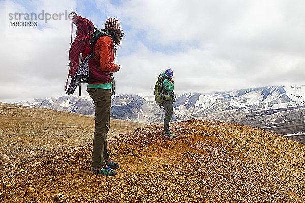 Zwei Frauen auf Rucksacktour mit Blick auf den Mount Katmai von den regenbogenfarbenen Bimsstein-  Fels- und Lehmhängen des Broken Mountain  Valley of Ten Thousand Smokes  Südwest-Alaska; Alaska  Vereinigte Staaten von Amerika