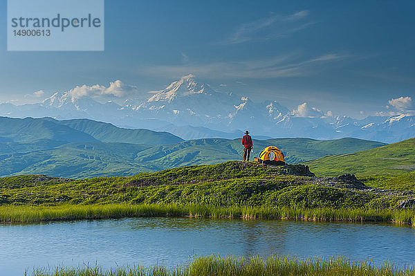 Rucksacktourist steht neben seinem Zelt in der Tundra und überblickt die Südseite des Denali und die Alaska Range  Denali State Park  Süd-Zentral-Alaska; Alaska  Vereinigte Staaten von Amerika