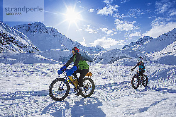 Zwei Frauen beim Fatbiking vor dem Skookum-Gletscher  Chugach National Forest  Alaska an einem sonnigen Wintertag  Süd-Zentral-Alaska; Alaska  Vereinigte Staaten von Amerika