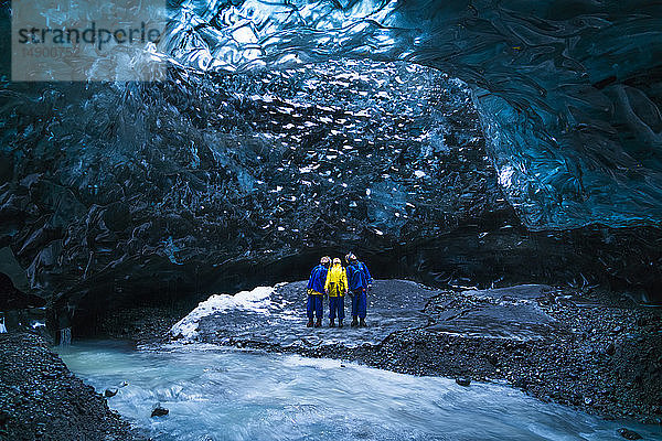 Gruppe von Menschen  die bei der Erkundung eines Gletschers in einer Eishöhle stehen; Island