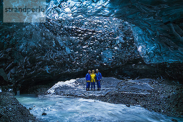Gruppe von Menschen  die bei der Erkundung eines Gletschers in einer Eishöhle stehen; Island