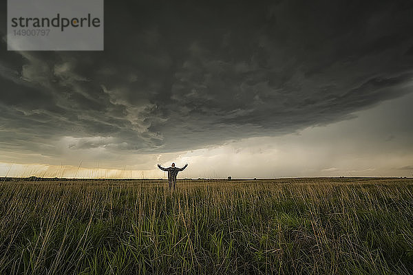 Dramatischer Himmel über der Landschaft während einer Sturmjagd im Mittleren Westen der Vereinigten Staaten. Mann steht auf dem Feld und beobachtet den herannahenden Sturm; Kansas  Vereinigte Staaten von Amerika
