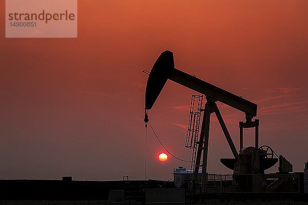 Silhouette eines Pumpjacks mit einem glühend warmen Sonnenball im Hintergrund  westlich von Airdrie; Alberta  Kanada