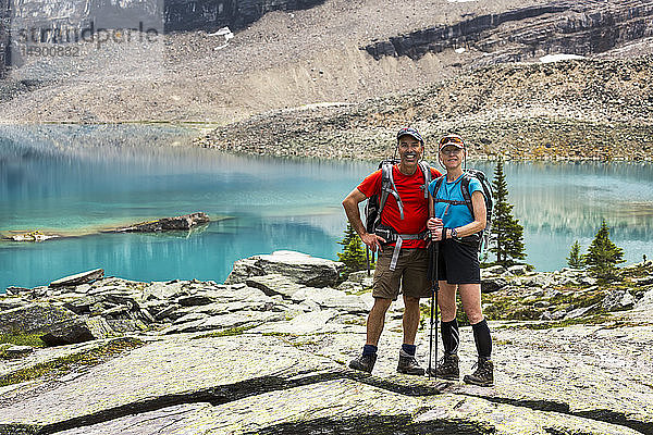 Eine Wanderin und ein Wanderer stehen in einem großen felsigen Gebiet mit einem farbenfrohen Alpensee und Bergklippen im Hintergrund; British Columbia  Kanada