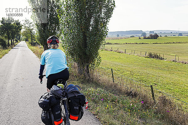 Radfahrerin auf einem bewaldeten Radweg mit Feldern in der Ferne  nördlich von Bastogne; Belgien