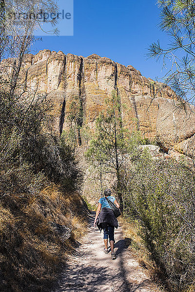 Eine Frau wandert auf dem Balconies Cave Trail unterhalb massiver Klippen im Pinnacles National Park; Kalifornien  Vereinigte Staaten von Amerika