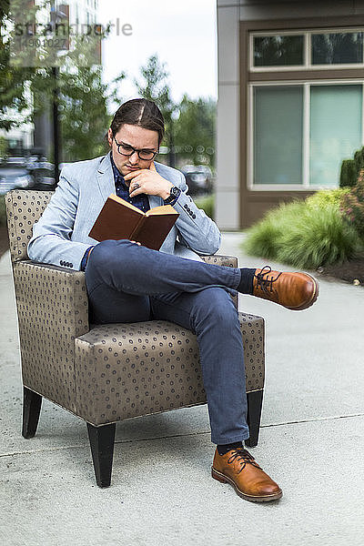Ein junger Mann sitzt in einem Sessel auf einer Veranda und liest ein Buch; Bothell  Washington  Vereinigte Staaten von Amerika