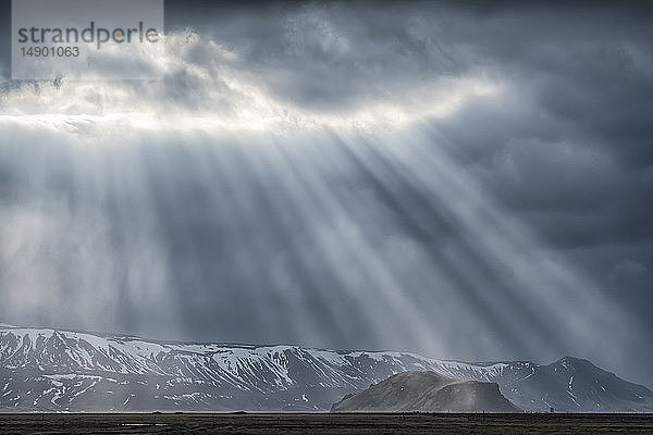 Dramatische Sonnenstrahlen dringen durch die Wolken an der Südküste Islands und schaffen ein beeindruckendes Bild; Island