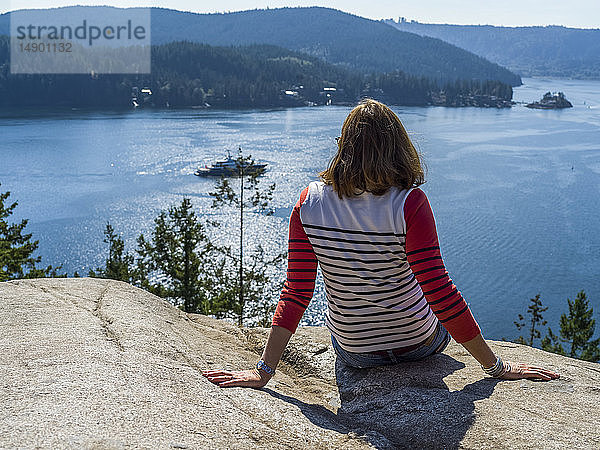 Eine Frau sitzt am Quarry Rock auf dem Baden-Powell Trail und blickt auf die Küste  Deep Cove  North Vancouver; Vancouver  British Columbia  Kanada