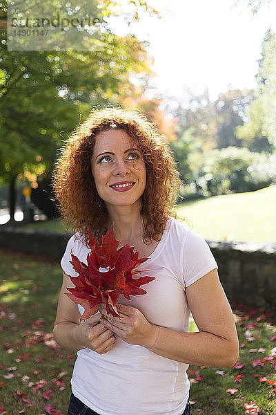 Porträt einer Frau mit rotem  lockigem Haar  die herbstlich gefärbte Blätter hält; Burnaby  British Columbia  Kanada