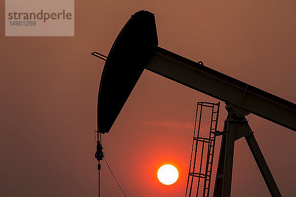 Silhouette eines Pumpjacks mit einem glühend warmen Sonnenball im Hintergrund  westlich von Airdrie; Alberta  Kanada