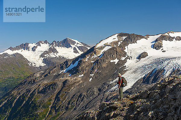 Ein Mann wandert in der Nähe des Harding Icefield Trail mit den Kenai Mountains und einem unbenannten Hängegletscher im Hintergrund  Kenai Fjords National Park  Kenai Peninsula  Süd-Zentral-Alaska; Alaska  Vereinigte Staaten von Amerika