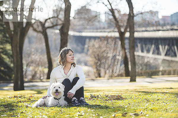 Frau sitzt mit ihrem Hund im Gras in einem Park mit der Skyline der Stadt im Hintergrund; Edmonton  Alberta  Kanada