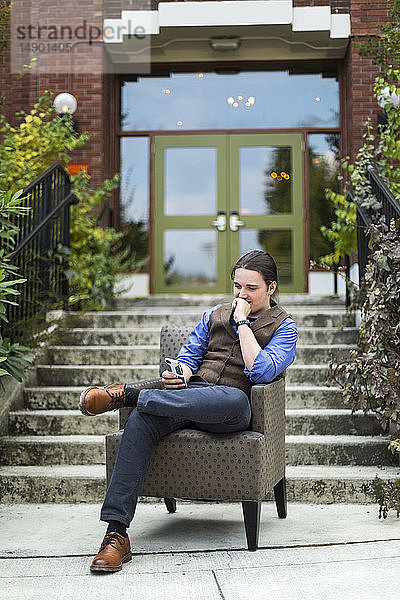 Ein junger Mann sitzt in einem Sessel im Freien und benutzt sein Smartphone; Bothell  Washington  Vereinigte Staaten von Amerika