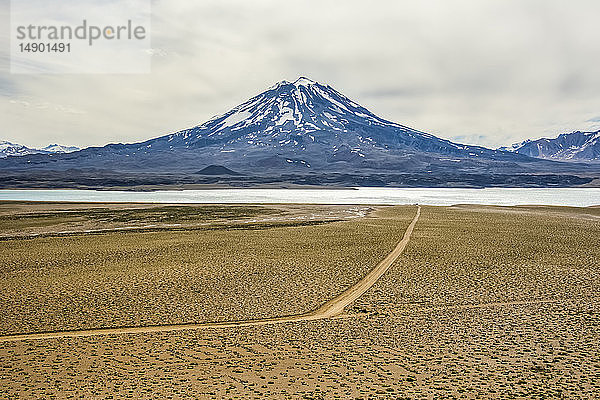 Vulkan hinter einem See in den Anden. Eine Schotterstraße führt das Auge ins Bild; Mendoza  Argentinien