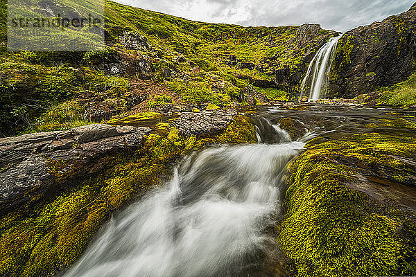 Wasser  das von einer felsigen Klippe in einen darunter liegenden Bach fällt; Island