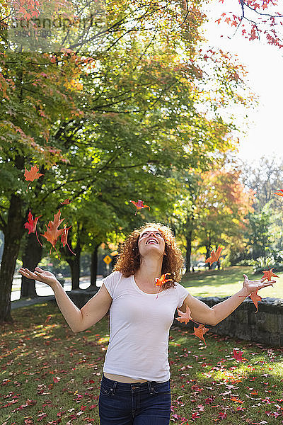 Porträt einer Frau mit rotem  lockigem Haar  die herbstlich gefärbte Blätter in die Luft wirft; Burnaby  British Columbia  Kanada