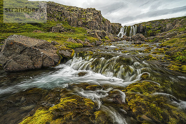 Wasser  das von einer felsigen Klippe in einen darunter liegenden Bach fällt; Island