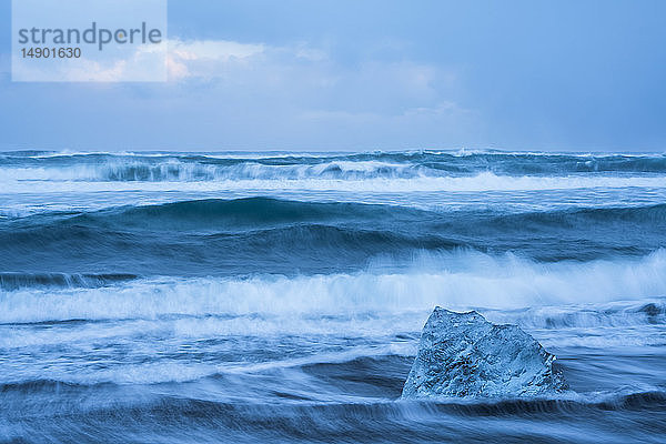 Das Meer umspült einen Eisbrocken an der Südküste Islands bei Jokulsarlon; Island