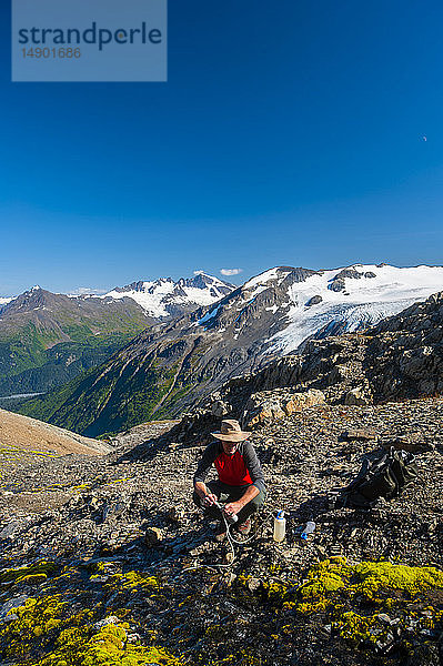 Ein Mann filtert Wasser beim Wandern auf dem Harding Icefield Trail im Kenai Fjords National Park mit einem Hängegletscher im Hintergrund; Alaska  Vereinigte Staaten von Amerika