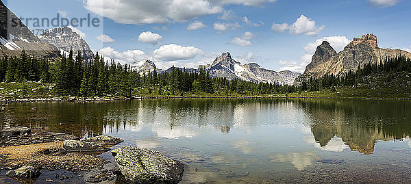 Bergkette  die sich in einem Alpensee mit felsigem Ufer und blauem Himmel und Wolken spiegelt; British Columbia  Kanada