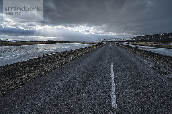 Straße  die in die dramatische Landschaft Islands führt  während die Sonne durch die Wolken scheint und ein schönes Bild abgibt; Island