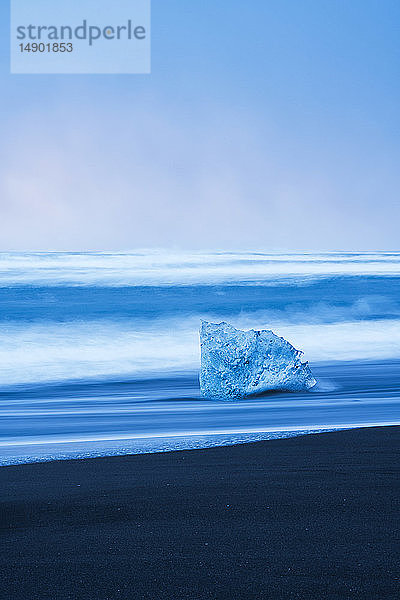 Eisbrocken am Ufer des Ozeans mit Wellen  die gegen die Küstenlinie schlagen; Island