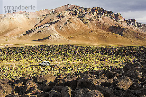 Ein Wohnmobil ist in der Weite eines Hochtals in den Anden geparkt. Die Berge in der Ferne sind vom späten Tageslicht ockerfarben gefärbt; Mendoza  Argentinien