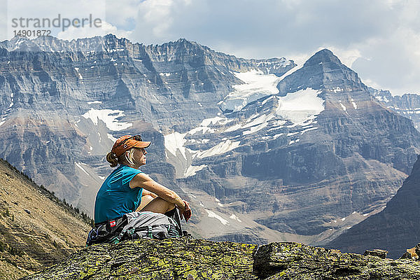 Wanderin auf einem Felsen sitzend mit Blick auf eine Berglandschaft im Hintergrund; British Columbia  Kanada