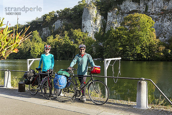 Weiblicher und männlicher Radfahrer stehen auf einem Radweg entlang eines Geländers am Flussufer mit Klippen im Hintergrund und blauem Himmel  südlich von Namur; Belgien