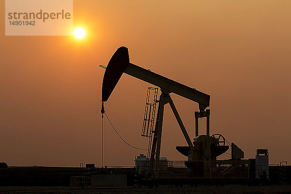 Silhouette eines Pumpjacks mit einem glühend warmen Sonnenball im Hintergrund  westlich von Airdrie; Alberta  Kanada