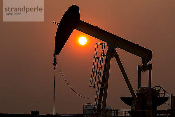 Silhouette eines Pumpjacks mit einem glühend warmen Sonnenball im Hintergrund  westlich von Airdrie; Alberta  Kanada