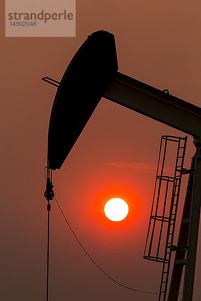 Silhouette eines Pumpjacks mit einem glühend warmen Sonnenball im Hintergrund  westlich von Airdrie; Alberta  Kanada