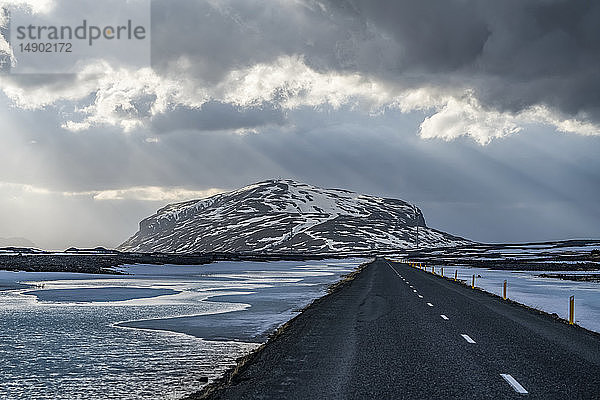 Straße  die in die dramatische Landschaft Islands führt  während die Sonne durch die Wolken scheint und ein schönes Bild abgibt; Island