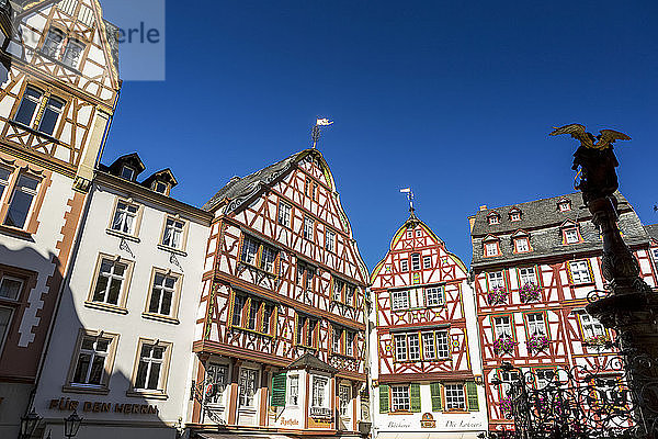 Dekorative mittelalterliche Gebäude auf dem Dorfplatz mit der Silhouette eines Engelsbrunnens und tiefblauem Himmel; Bernkastel  Deutschland