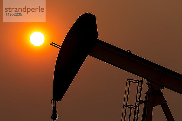 Silhouette eines Pumpjacks mit einem glühend warmen Sonnenball im Hintergrund  westlich von Airdrie; Alberta  Kanada