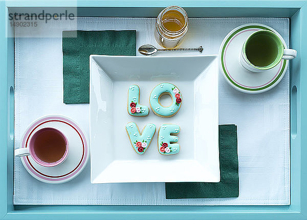 Tee in Tassen mit Untertassen und Kekse mit der Aufschrift Liebe auf einem Tablett