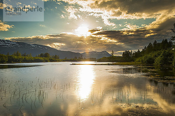 Das ruhige Wasser eines unbenannten Sees im Portage Valley an einem sonnigen Sommerabend  während die Sonne in Süd-Zentral-Alaska untergeht; Alaska  Vereinigte Staaten von Amerika