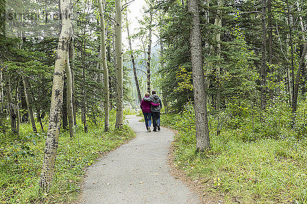 Ein reifes Paar  das auf einem Wanderweg spazieren geht und die Arme umeinander legt; Kananaskis  Alberta  Kanada